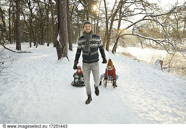 Mid adult father with sons sitting on sled during winter