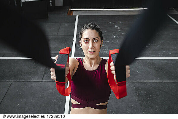 Mid adult female athlete pulling resistance band while exercising in gym