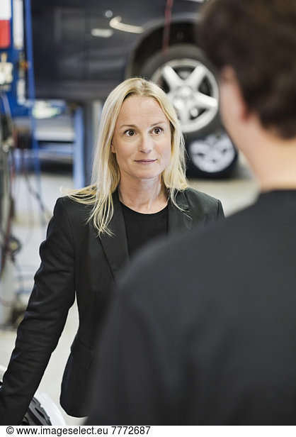 Mid adult female customer looking at mechanic in auto repair shop