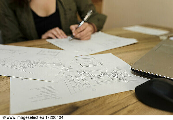Mid adult female design professional making drawing on paper while sitting at desk in industry