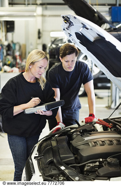 Mid adult female mechanic holding digital tablet while discussing with coworker over car engine