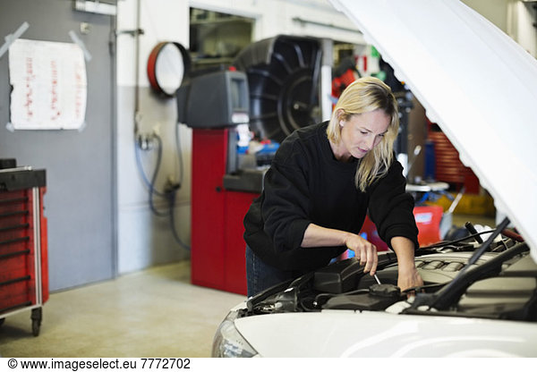 Mid adult female mechanic repairing car engine at auto repair shop
