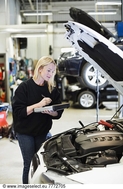 Mid adult female mechanic using digital tablet while analyzing car engine