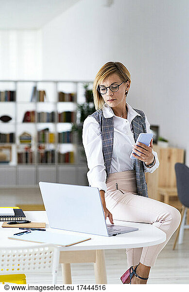 Mid adult female professional using laptop while sitting on desk in office