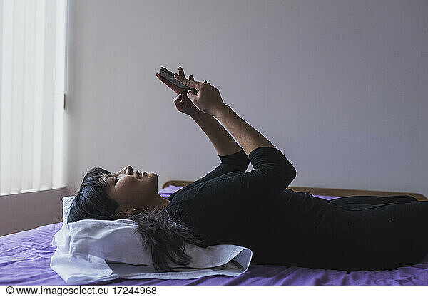 Mid Adult Frau Text-Messaging auf Smartphone im Schlafzimmer