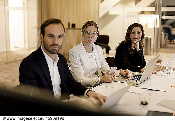Mid adult male and female professionals listening in meeting while sitting at conference table in office