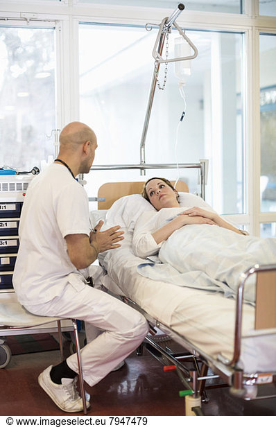 Mid adult male doctor communicating with patient lying on bed in hospital ward