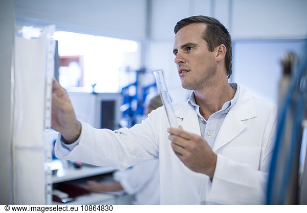 Mid adult man adjusting laboratory equipment  holding test tube