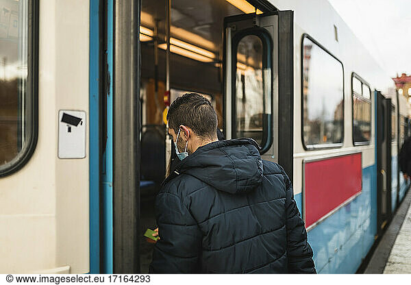 Mid adult man boarding tram during pandemic