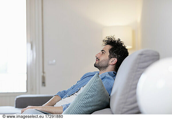 Mid adult man day dreaming while sitting on sofa in living room
