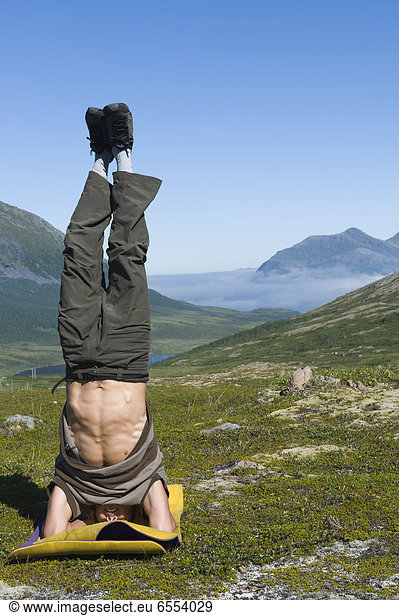 Mid adult man doing headstand  mountains in background