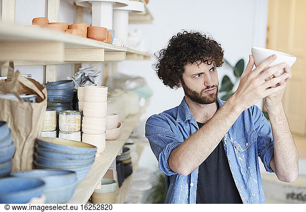 Mid adult man examining bowl in pottery class