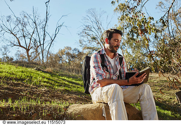 Mid adult man hiking, sitting on boulder reading book