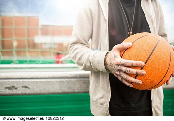 Mid adult man holding basketball  mid section