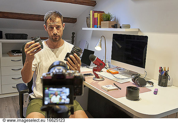 Mid adult man holding camera lenses while sitting at home