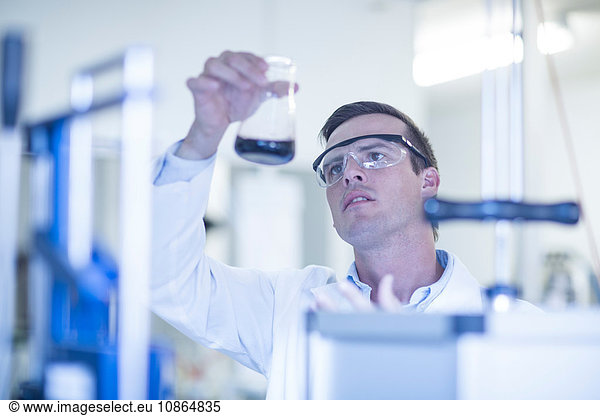 Mid adult man in laboratory  looking at liquid in glass flask
