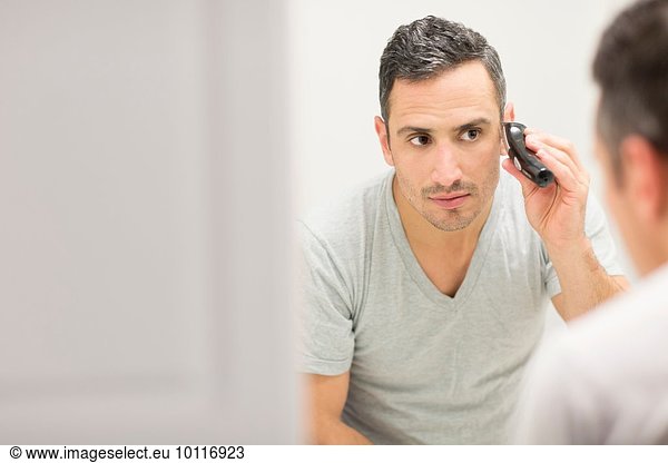 Mid adult man  looking in mirror  using electric shaver