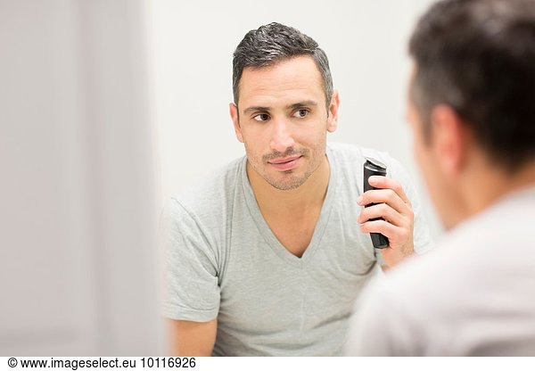 Mid adult man  looking in mirror  using electric shaver