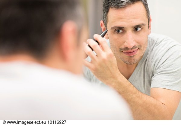 Mid adult man  looking in mirror  using tweezers