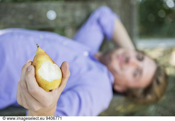 Mid adult man lying on bench and eating pear