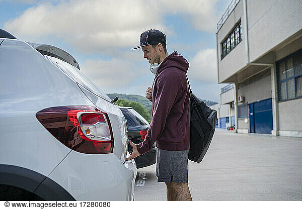 Mid adult man opening car trunk while standing at parking lot