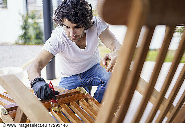 Mid adult man painting wooden deck chair