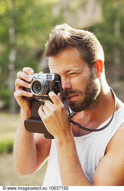 Mid adult man photographing through old-fashioned camera in forest