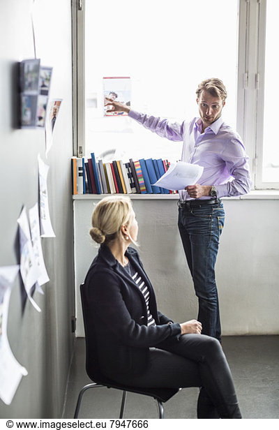 Mid adult man pointing on photograph while discussing with female colleague in office