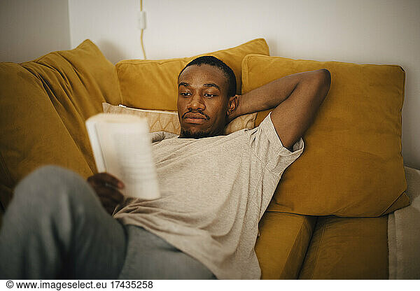 Mid adult man reading book while lying on sofa at home