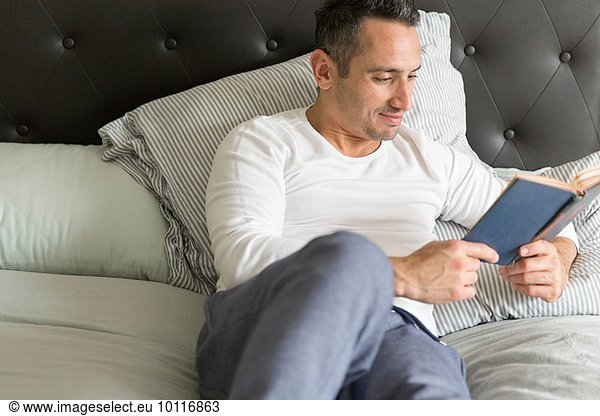 Mid adult man  relaxing on bed  reading book