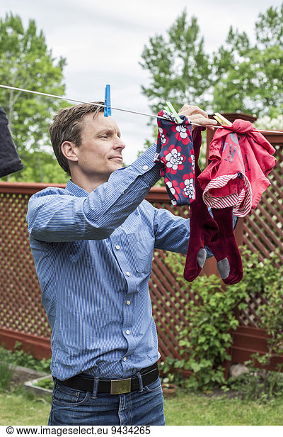 Mid adult man removing clothes from clothesline at yard