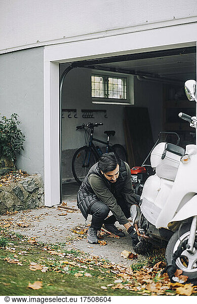 Mid adult man repairing motor scooter in garage at back yard
