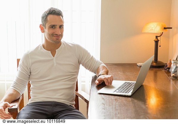 Mid adult man sitting at desk  using laptop