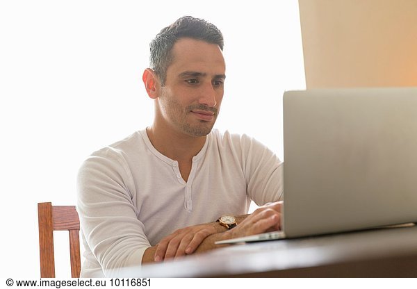 Mid adult man sitting at desk  using laptop