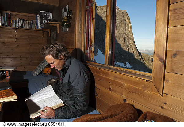 Mid adult man sitting in mountain cabin and reading book