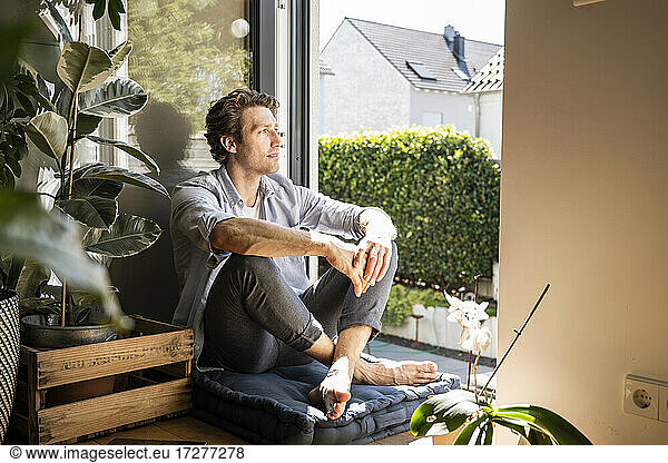 Mid adult man sitting on cushion at home on sunny day