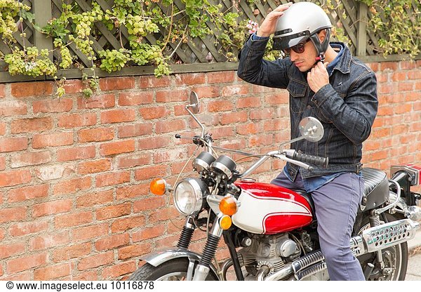 Mid adult man  sitting on motorbike  putting on helmet