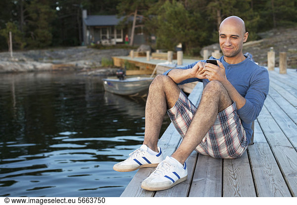 Mid adult man sitting on pier sending text message