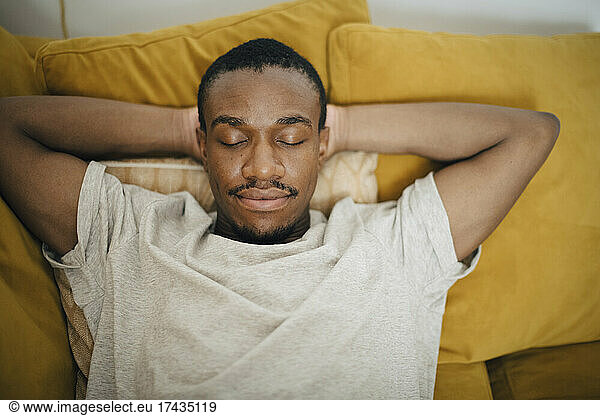 Mid adult man sleeping with hands behind head on sofa in living room