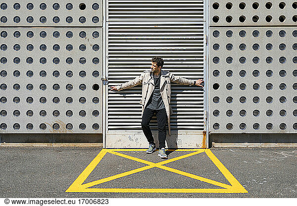 Mid adult man standing in yellow marked area in front of concrete wall  with arms outstretched
