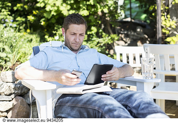 Mid adult man using digital tablet while relaxing on lounge chair at yard