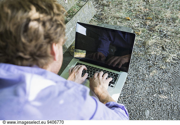 Mid adult man using laptop on bench