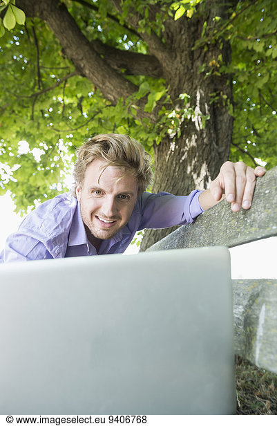 Mid adult man using laptop on bench  smiling