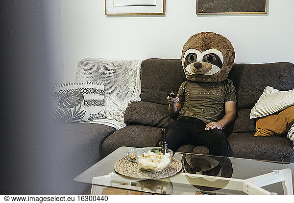 Mid adult man wearing teddy bear mask watching TV while sitting in living room