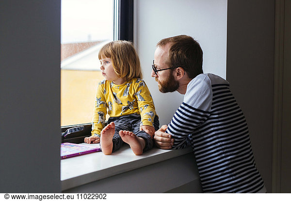 Mid adult man with daughter looking through window at home