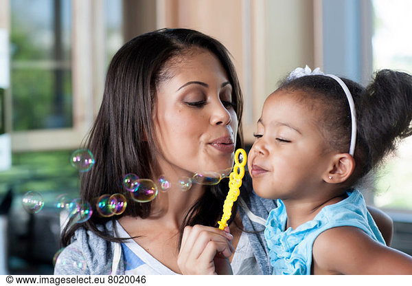 Mid adult mother and young girl blowing bubbles  close up