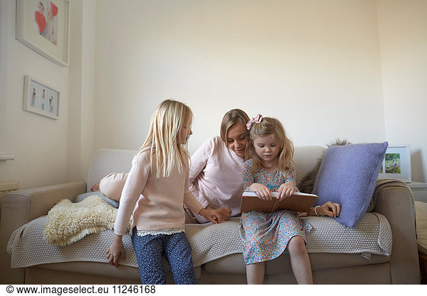 Mid adult woman and daughters reading storybook on sofa