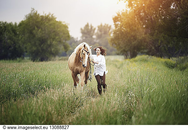 Mid adult woman and horse running on grassy field at countryside