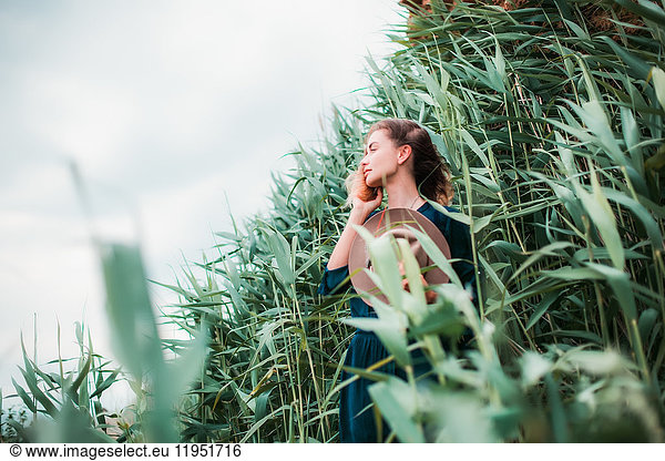 Mid adult woman beside long grass,  touching hair,  breathing in fresh air