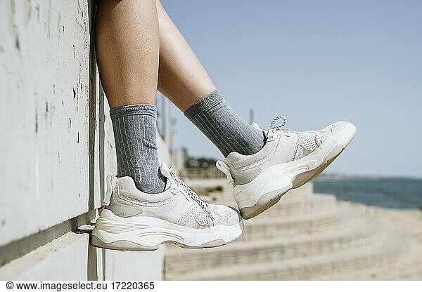 Mid adult woman dangling feet while sitting on retaining wall